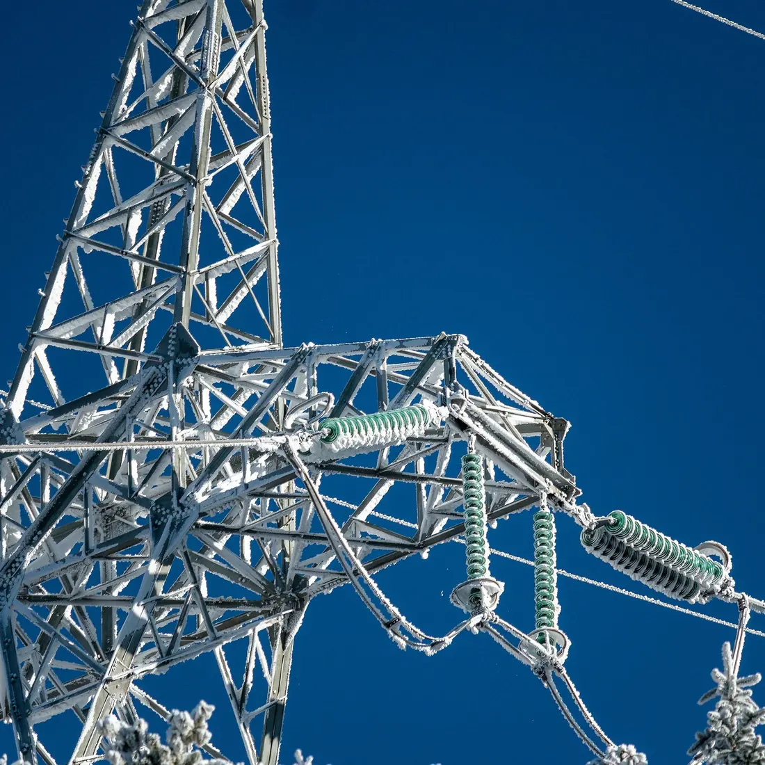 Frost-covered transmission tower under a blue sky